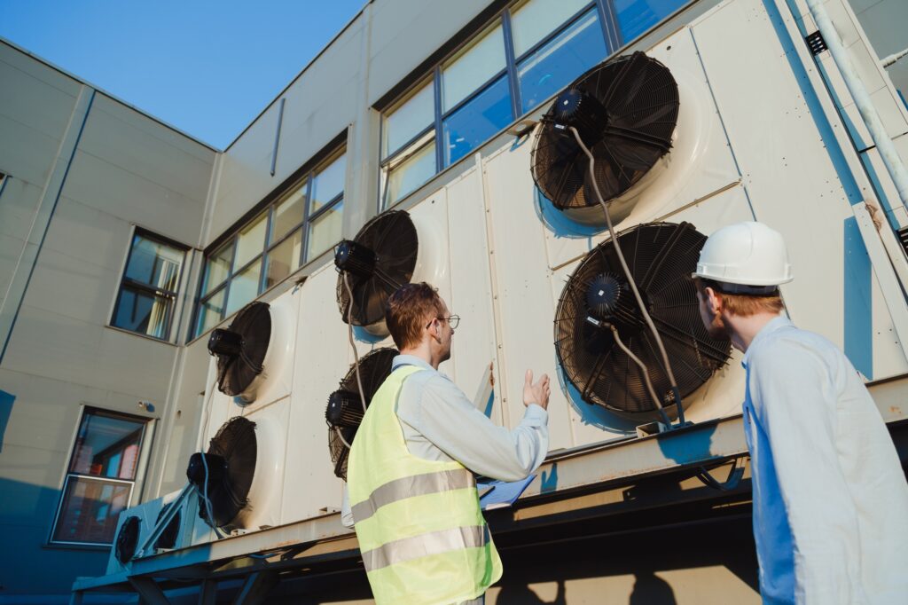 Service engineers in uniform inspecting industrial refrigeration system, outdoor refrigeration plant